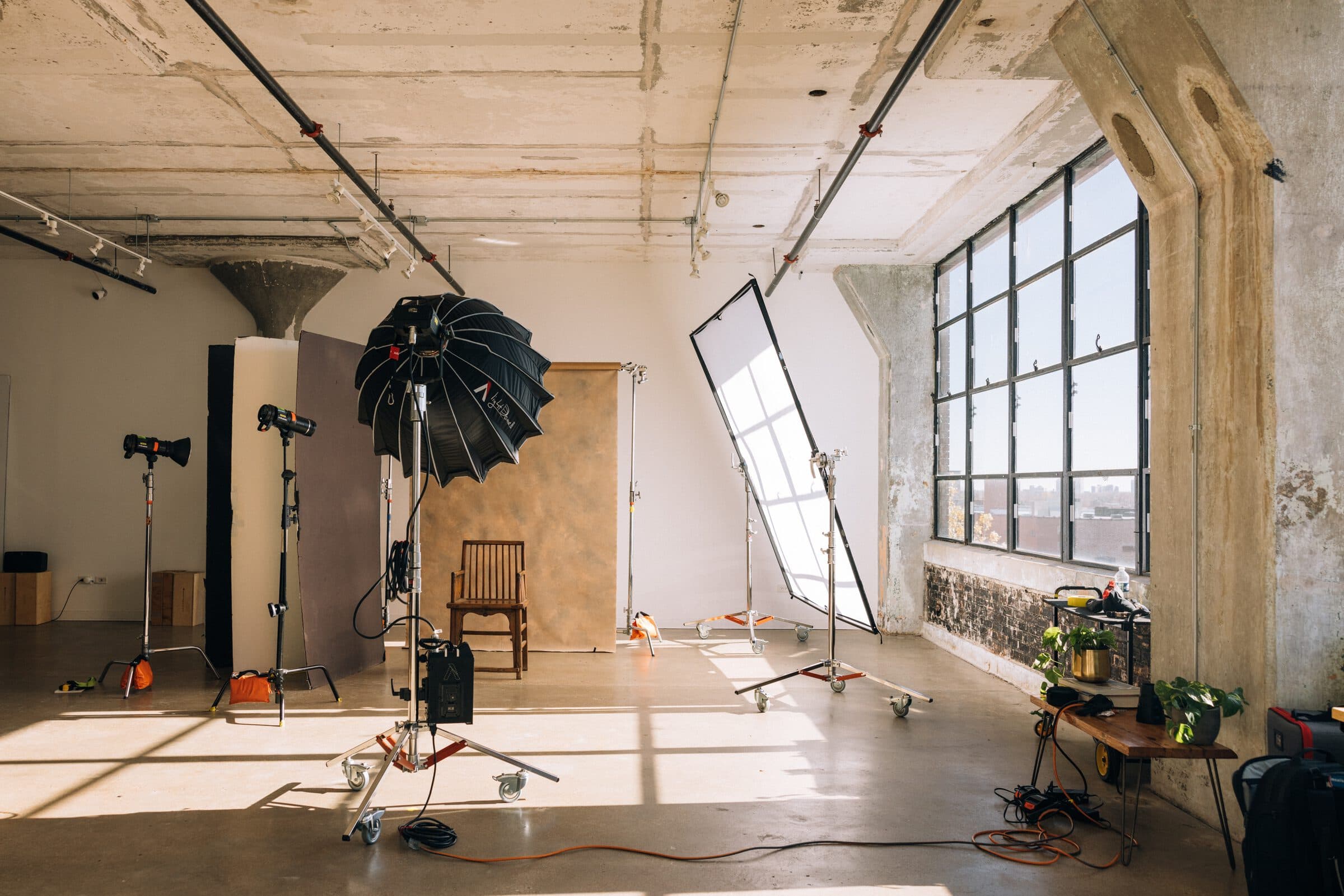 A portrait set from an AIR residency: a wooden chair against a painted canvas backdrop, a large softbox and strobes, and sun from the windows across the floor
