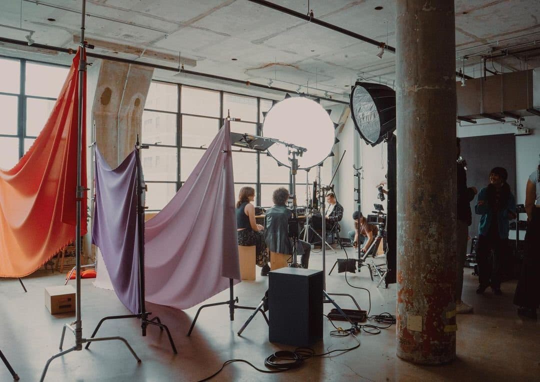 A crew setting up draped fabric backdrops and lights in front of the windows